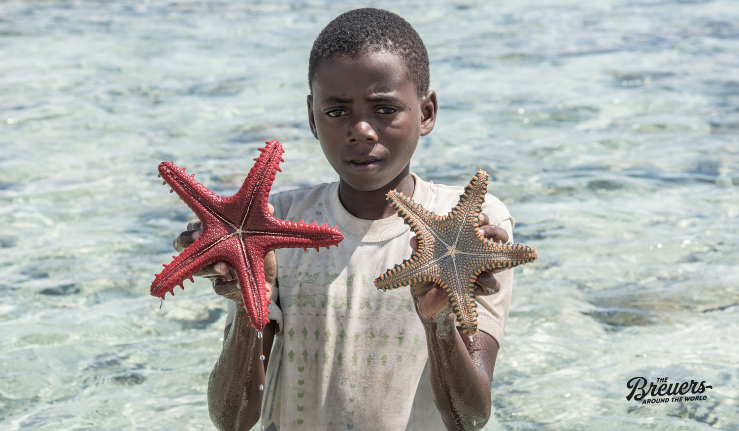 Kleiner Junge hält Seesterne in der Hand am Strand von Zanzibar